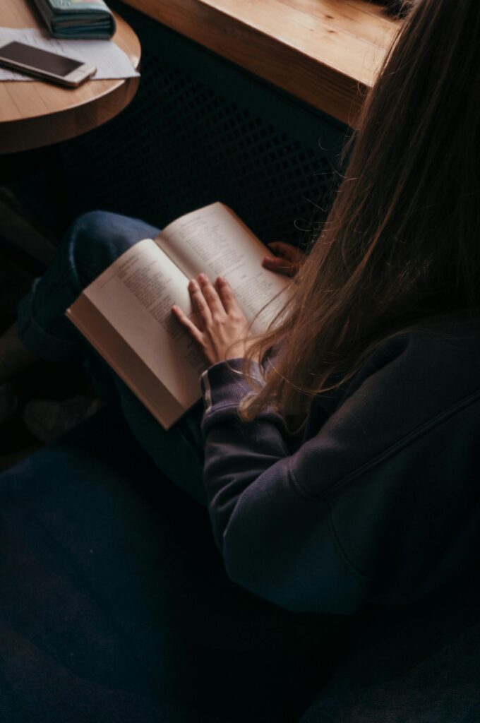 pexels-photo-2942194-2942194 A young woman reading a book in a cozy indoor setting by the window.